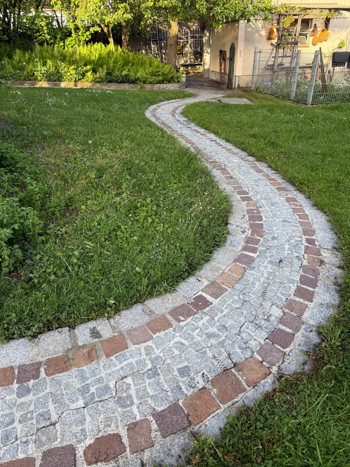 Geschwungener Gartenweg aus grauem und rotem Granitpflaster nach der Reinigung